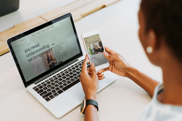 A woman is using her phone to look at a website on a laptop.